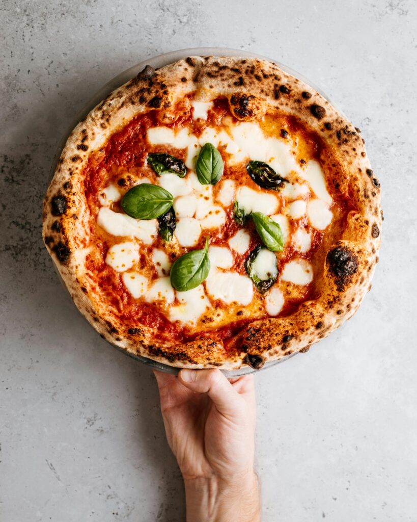 Close-up of a fresh Margherita pizza with mozzarella and basil, held over a gray background.
